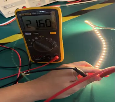 Digital multimeter showing 21.60V at the end of an anonymous 5m 24V LED strip